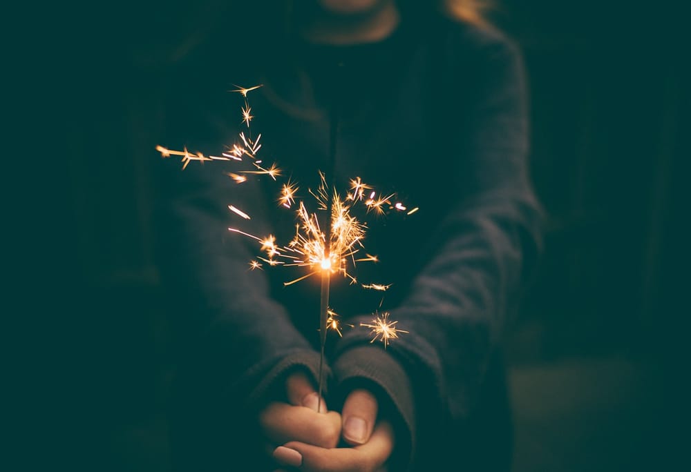 Person in shadow holds a sparkler in both hands.