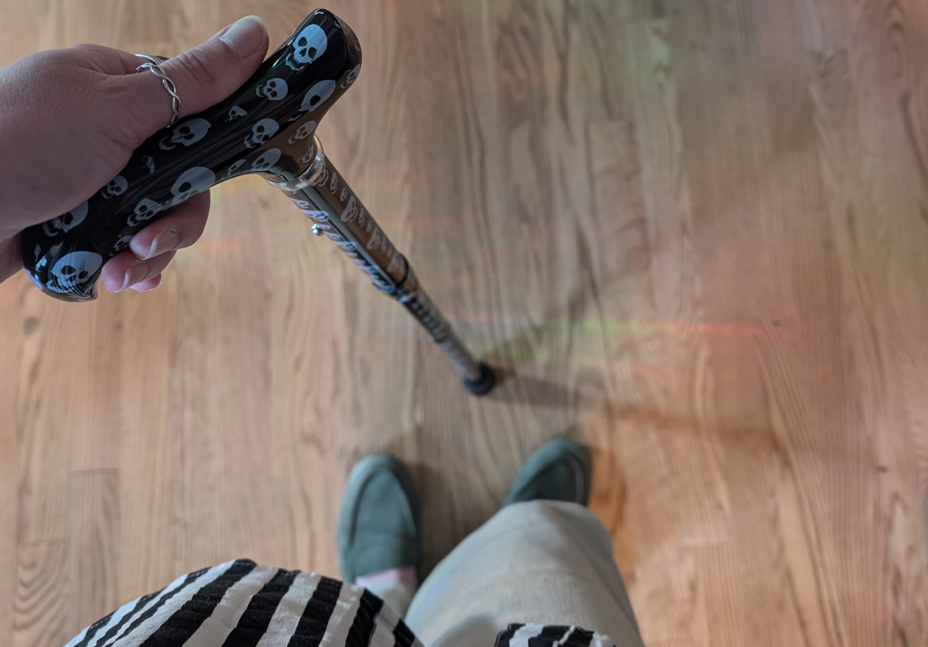 Shot of person's hand holding cane with black and white skull pattern on hard wood floor