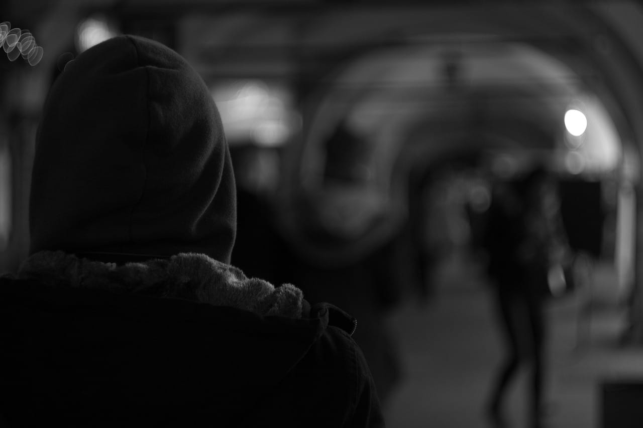 Black and white photo of person in jacket and hood facing away from camera with blurry background